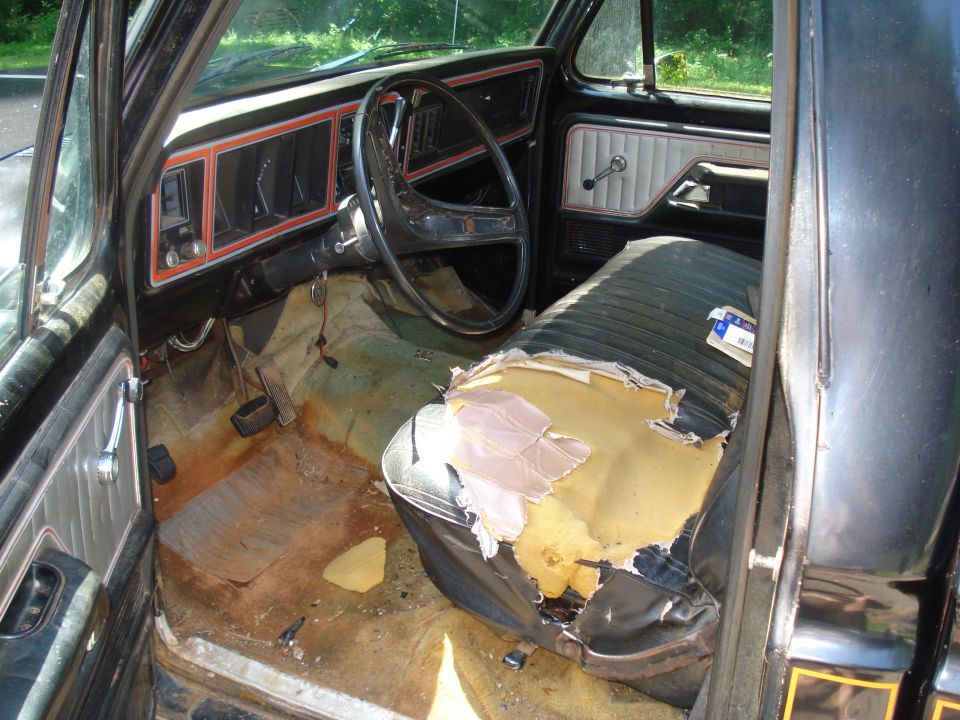 Interior of a 1977 Ford F-100 showing worn driver's seat and dashboard