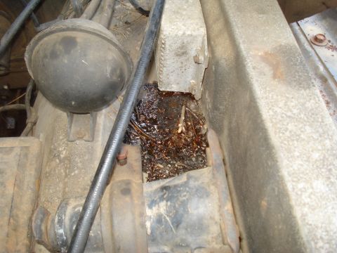 1984 Ford F-250 - An engine bay displays a leak of dark, oily fluid mixed with debris.