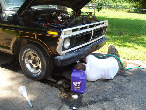 1984 Ford F-250 - A person works on the engine of a black 1977 Ford truck, which has its hood propped open.