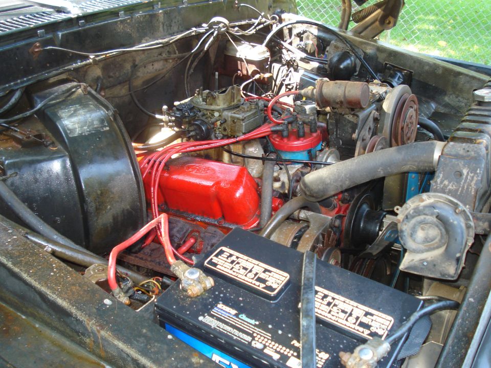 Engine bay showing V8 engine, carburetor, distributor, battery, and radiator hose
