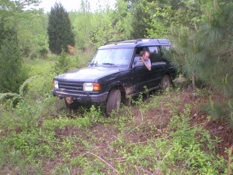 1983 Ford Bronco - A black Land Rover Discovery navigates a wooded, off-road trail with a driver visible through the window.