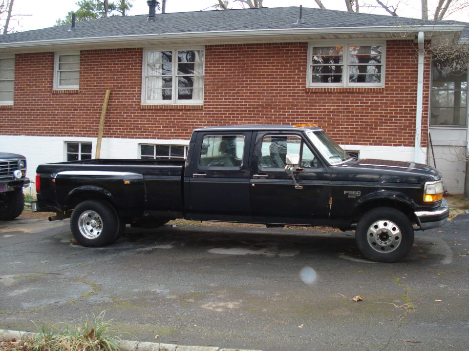 Black crew cab dually pickup truck parked on asphalt, side view. Visible front fender badge reads "F-350"