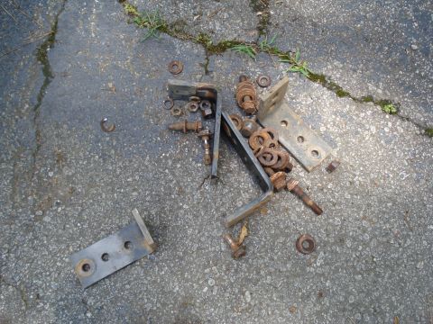 1994 Ford F-350 - Assorted rusty metal brackets, bolts, and washers are scattered on a cracked asphalt surface.