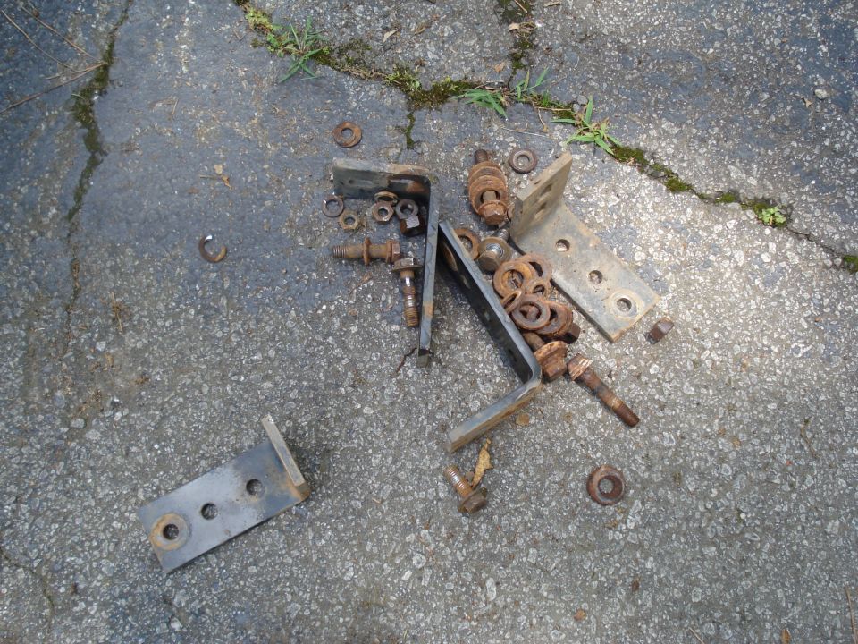Pile of rusty metal brackets, bolts, and washers on asphalt