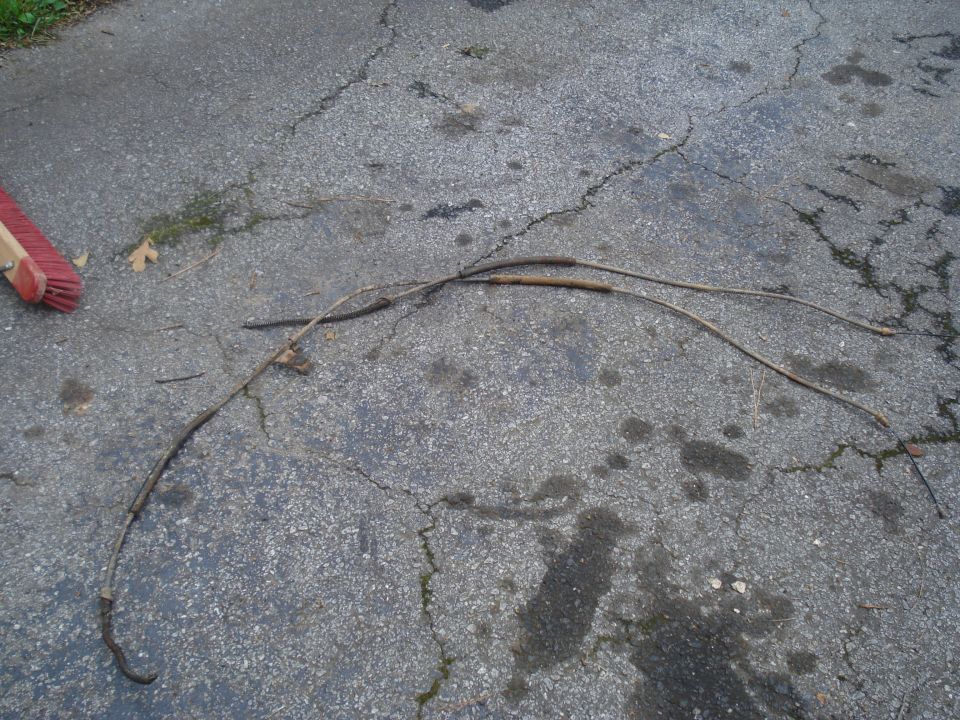 Two brake cables lying on cracked asphalt, with a red-bristled broom head visible on the left