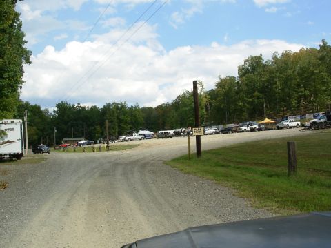 1983 Ford Bronco - A busy parking area with multiple vehicles, including an RV, trucks, and cars, surrounded by trees.