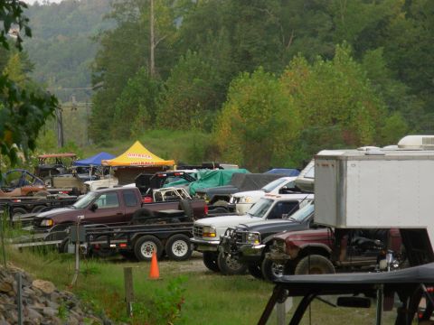 1983 Ford Bronco - A variety of trucks and vehicles are parked outdoors, some covered, under tents and trees.
