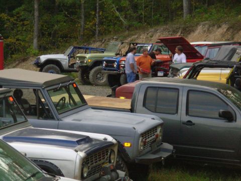 1983 Ford Bronco - Several vintage Ford Broncos are gathered in an outdoor lot, with people milling around.