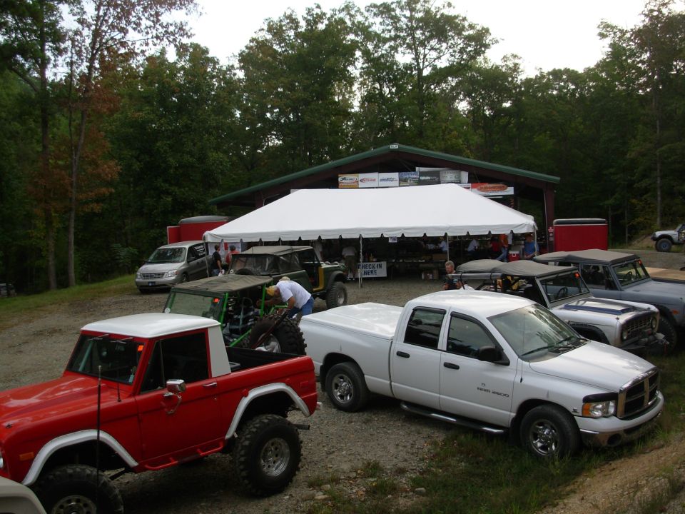 Red lifted early Ford Bronco half-cab and white Dodge Ram parked at an off-road event