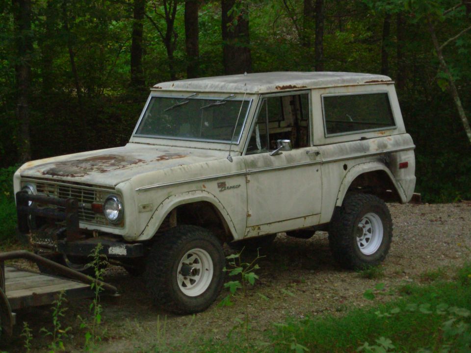 Rusty white early Ford Bronco hardtop with winch bumper and white steel wheels on gravel