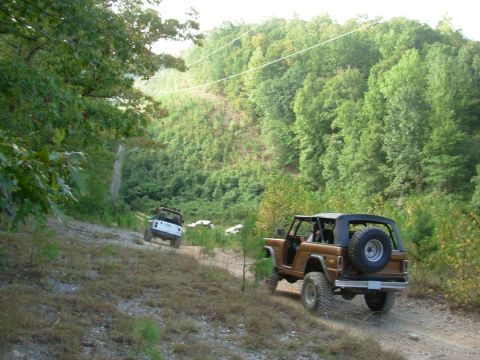 1983 Ford Bronco - Two off-road vehicles navigate a steep, wooded trail.