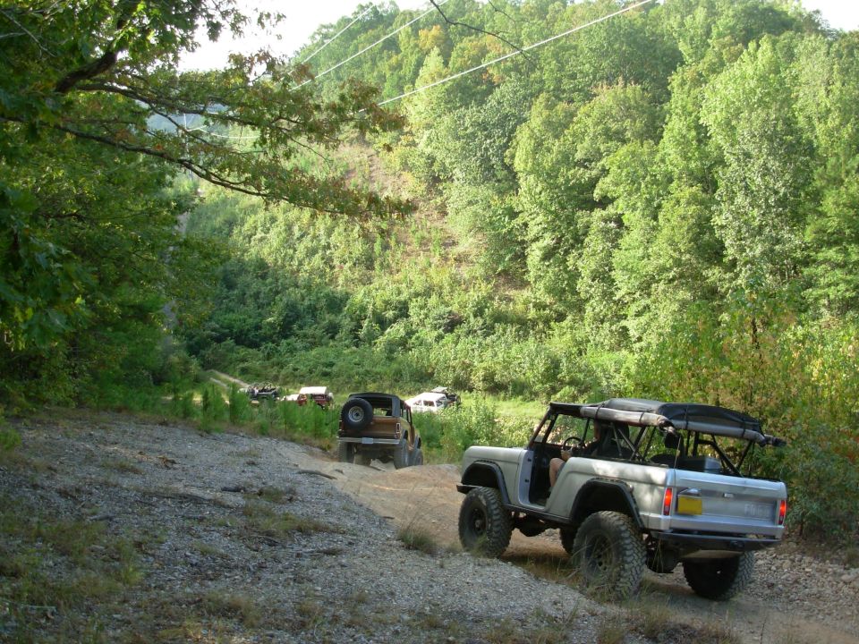 Silver open-top early Bronco on a rocky off-road trail with others ahead