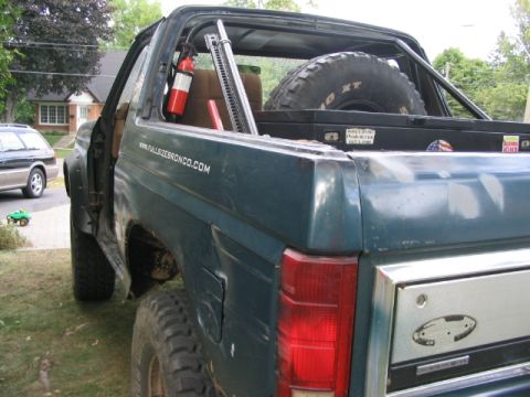 1986 Ford Bronco - Rear view of a dark teal Ford Bronco, equipped with a spare tire and safety equipment.