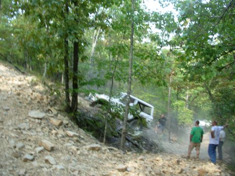 1983 Ford Bronco - A white SUV navigates a challenging off-road trail, with onlookers observing its progress.