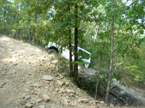 1983 Ford Bronco - A white SUV is partially obscured by trees as it navigates a steep, rocky trail.