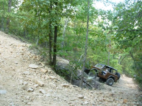 1983 Ford Bronco - A Jeep CJ-7 navigates a challenging, rocky trail through a wooded area.