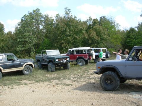 1983 Ford Bronco - A group of Ford Broncos are gathered outdoors on a sunny day, with people interacting near the vehicles.