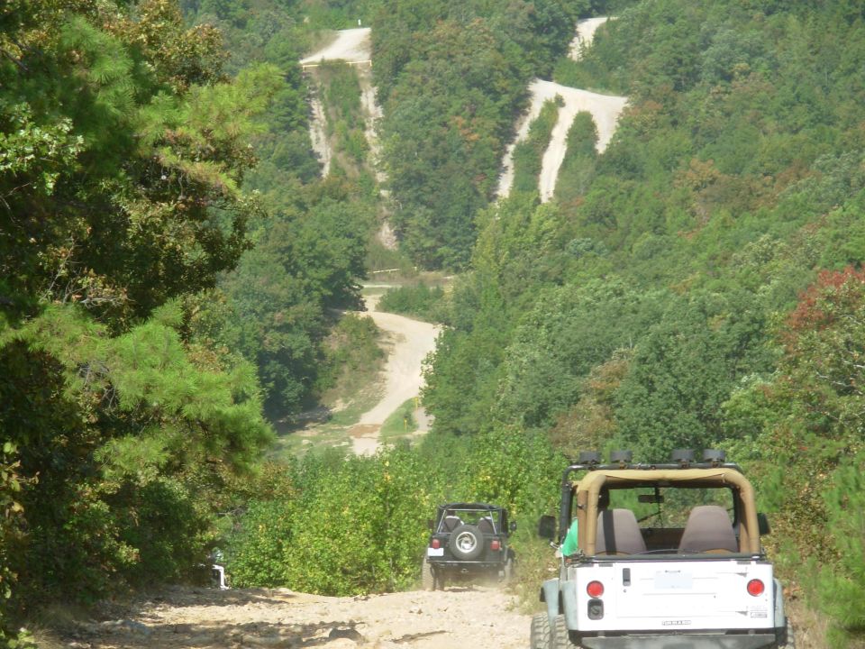 White topless Jeep Wrangler from the rear on a wooded off-road trail with hillside switchbacks
