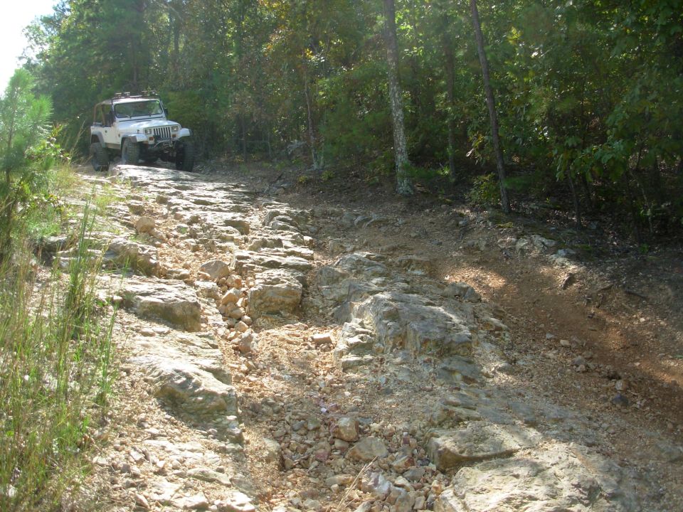 White Jeep Wrangler YJ at the top of a rocky rutted off-road trail in the woods