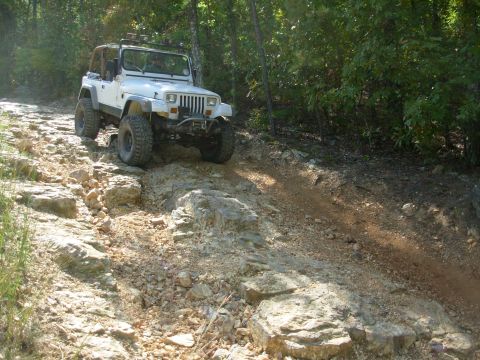 1983 Ford Bronco - A white Jeep Wrangler navigates a challenging, rocky terrain on an off-road trail.