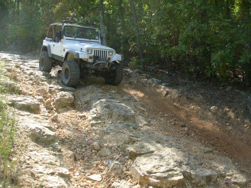 White square-headlight Jeep Wrangler with winch bumper descending a rocky wooded trail