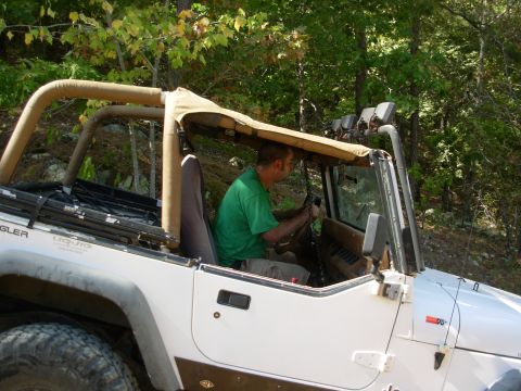 1983 Ford Bronco - Driver in a green shirt operates the steering wheel of a white Jeep Wrangler with a tan soft top.