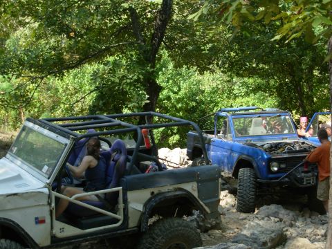 1983 Ford Bronco - Two Ford Broncos navigate a challenging off-road course, one with its hood open for inspection.