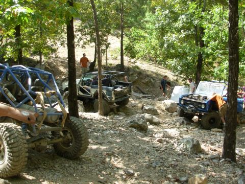 1983 Ford Bronco - Off-road vehicles tackle a challenging rocky path in a wooded area.