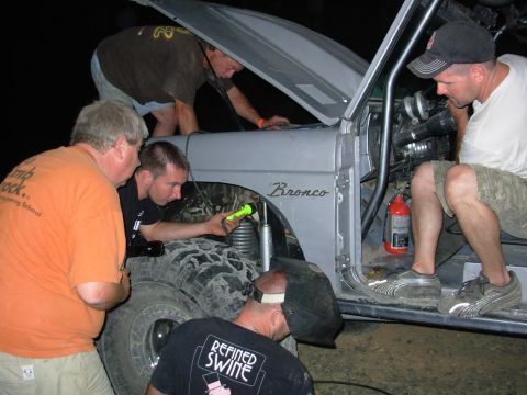 1983 Ford Bronco - A group of men are gathered around a Ford Bronco, some inspecting the engine and others working on it at night.