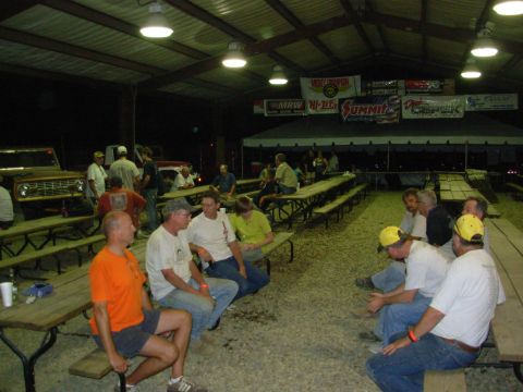 1983 Ford Bronco - A brown Ford Bronco is visible on the left side of the image, parked under a large covered area with picnic tables and people.