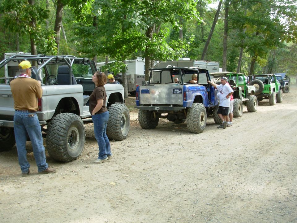 Row of lifted off-road rigs on a dirt trail, blue tube-chassis buggy in front