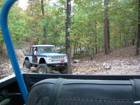 1983 Ford Bronco - This off-road SUV, likely a first-generation Ford Bronco, navigates a wooded trail with another vehicle visible in the background.
