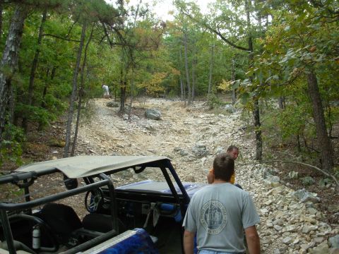 1983 Ford Bronco - Off-road vehicles navigate a challenging rocky trail through a forest.