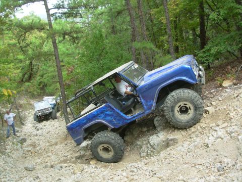 1983 Ford Bronco - Two SUVs navigate a challenging rocky off-road trail in a wooded area.