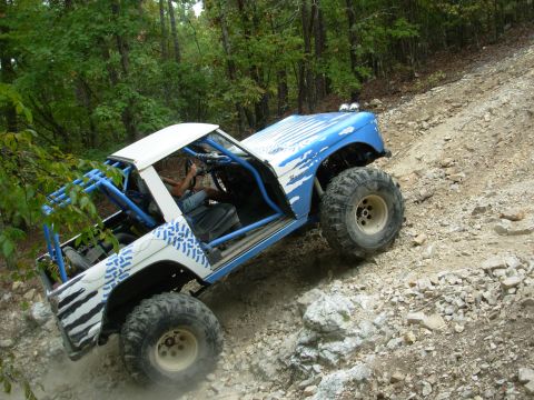 1983 Ford Bronco - Off-road SUV with custom paint and roll cage navigates a steep, rocky incline.