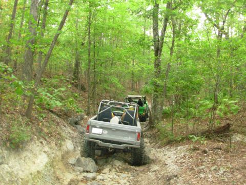 1983 Ford Bronco - This 1983 Ford Bronco navigates a challenging rocky trail through a wooded area, with another off-road vehicle following behind.
