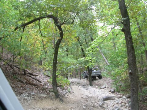 1983 Ford Bronco - An off-road vehicle navigates a challenging trail within a wooded area.
