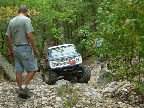 1983 Ford Bronco - A man watches a Ford Bronco navigate a challenging off-road trail through a wooded area.