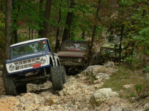 1983 Ford Bronco - Three Ford Broncos navigate a challenging rocky trail through a wooded area.