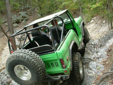 1983 Ford Bronco - Green off-road vehicle navigates a rocky trail with a spare tire mounted at the rear.