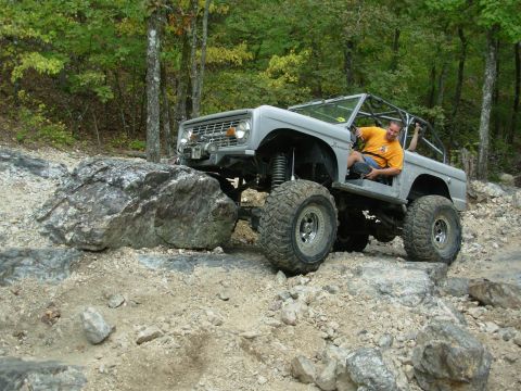 1983 Ford Bronco - A silver Ford Bronco navigates a rocky trail with a man in the driver's seat.