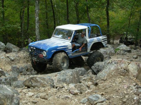 1983 Ford Bronco - Modified off-road vehicle tackles a challenging rocky trail with a driver inside.