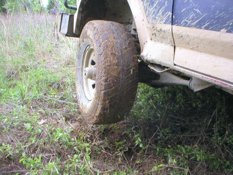 1983 Ford Bronco - A muddy 1983 Ford Bronco navigates off-road terrain, its side panel and wheel caked in dirt.