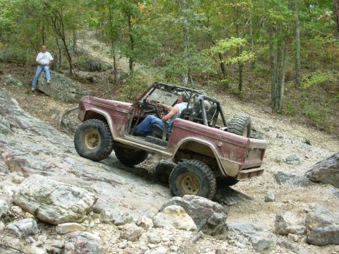 1983 Ford Bronco - A maroon Ford Bronco navigates a challenging rocky trail with a driver and passenger inside.