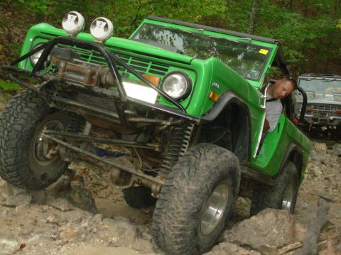 1983 Ford Bronco - A modified green Ford Bronco tackles a challenging rocky trail, with another Bronco visible behind it.
