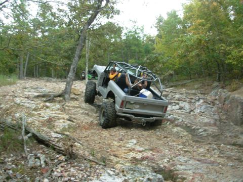 1983 Ford Bronco - This modified off-road vehicle navigates a challenging rocky path through a wooded area.