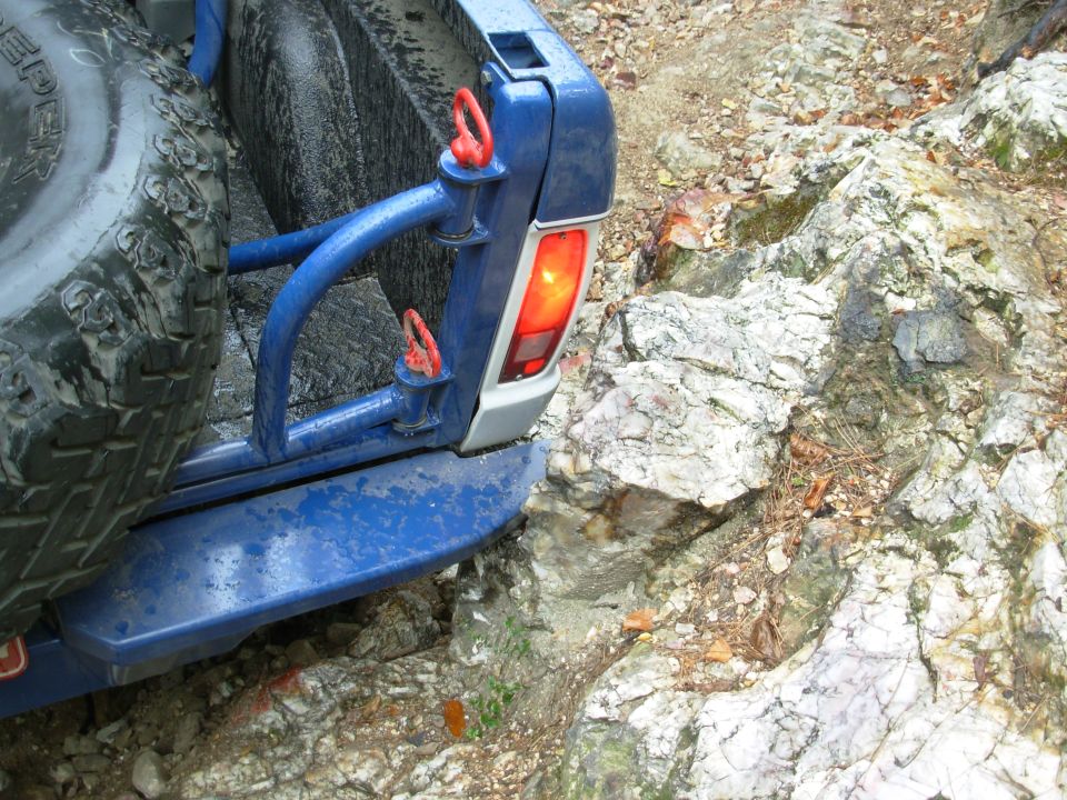 Blue 4x4 rear bumper with swing-out spare tire carrier and red latch on white rock