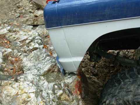 1983 Ford Bronco - The rear quarter panel of a blue and white Ford Bronco is shown navigating rocky terrain.