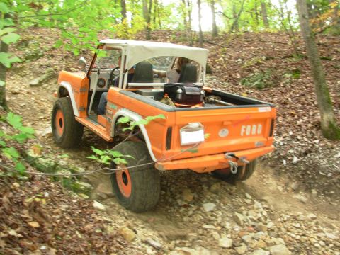 1983 Ford Bronco - Orange 1983 Ford Bronco navigates a rocky, wooded off-road path.