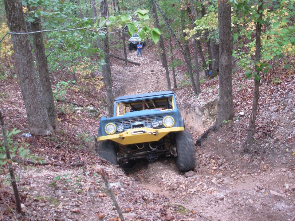 Teal classic Ford Bronco with yellow winch bumper descending a rutted rocky wooded trail
